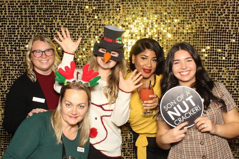Photo booth with a gold background with group of women posting at a corporate holiday event.