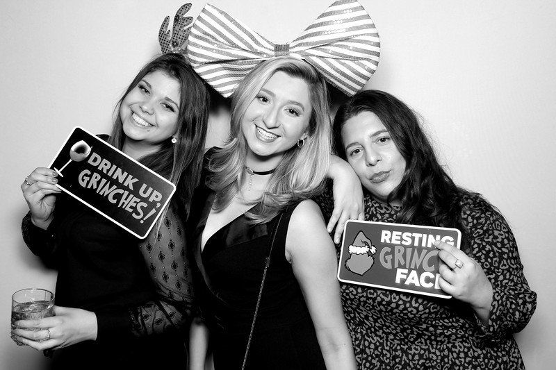 Three women posing in a photo booth; holding signs: 