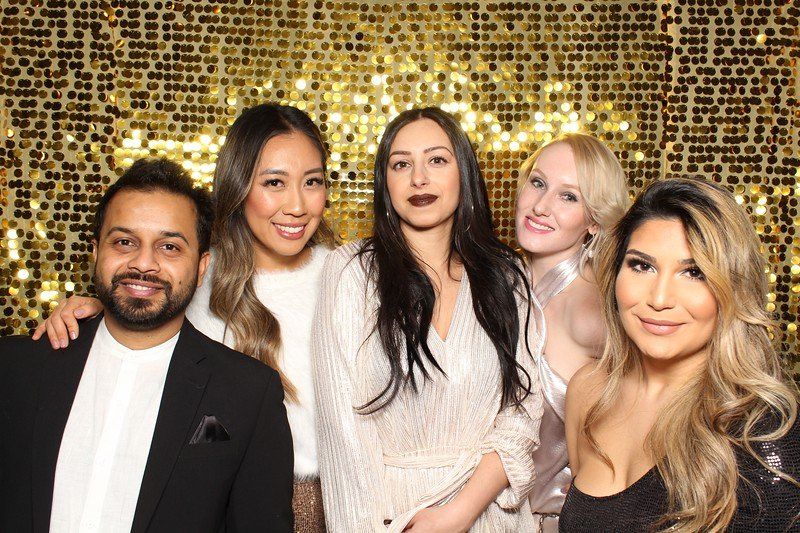Five people smiling, posing in front of a gold sequin backdrop.