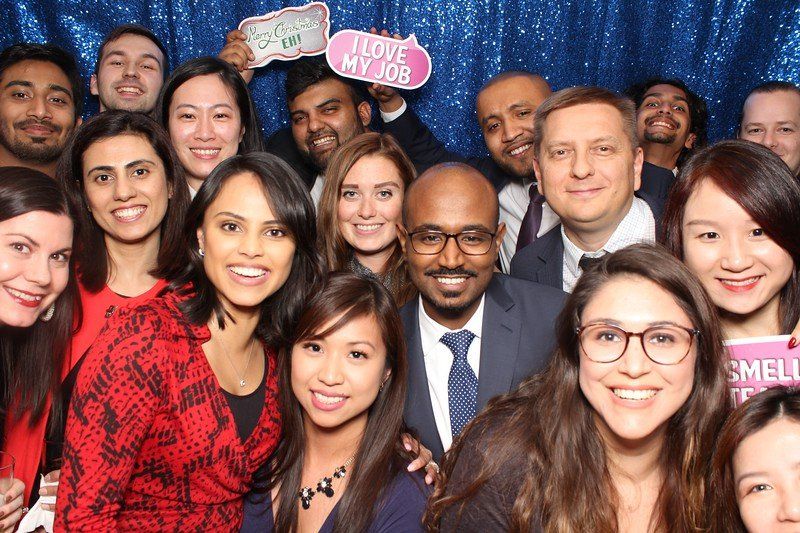 Group of smiling people posing for a photo in front of a blue sparkly backdrop.