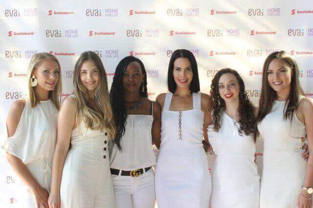 Six people posing in white outfits in front of a backdrop with logos.