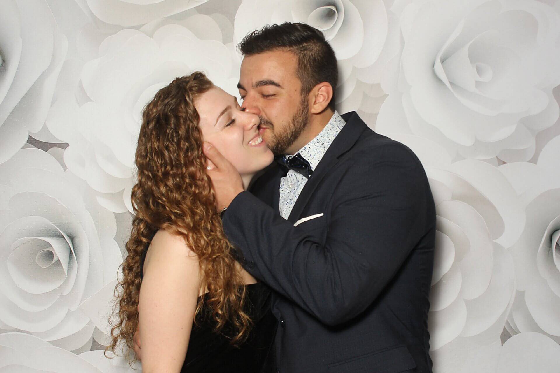 Man kissing woman's cheek; floral photo booth backdrop.