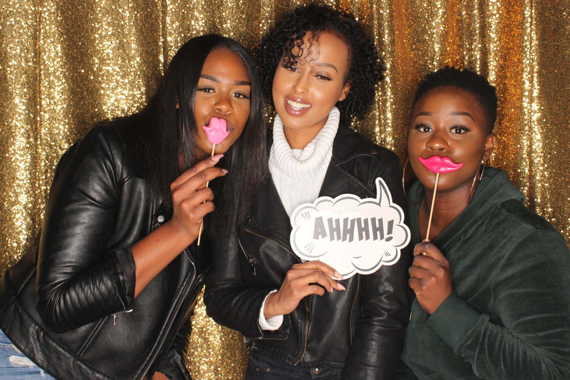 Three people posing with props in front of a gold backdrop; one holds 