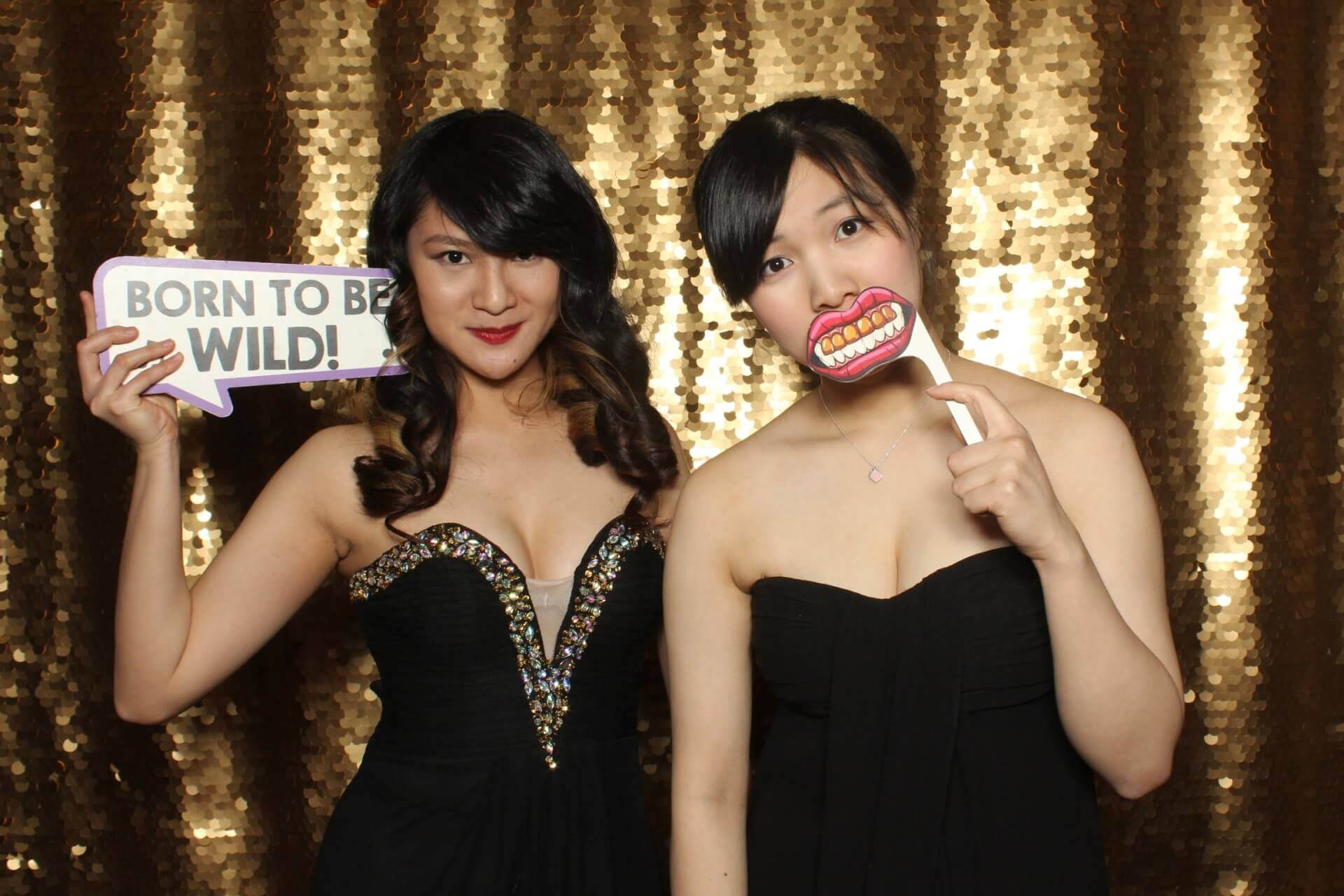 Two people pose for photo booth with props. One holds 
