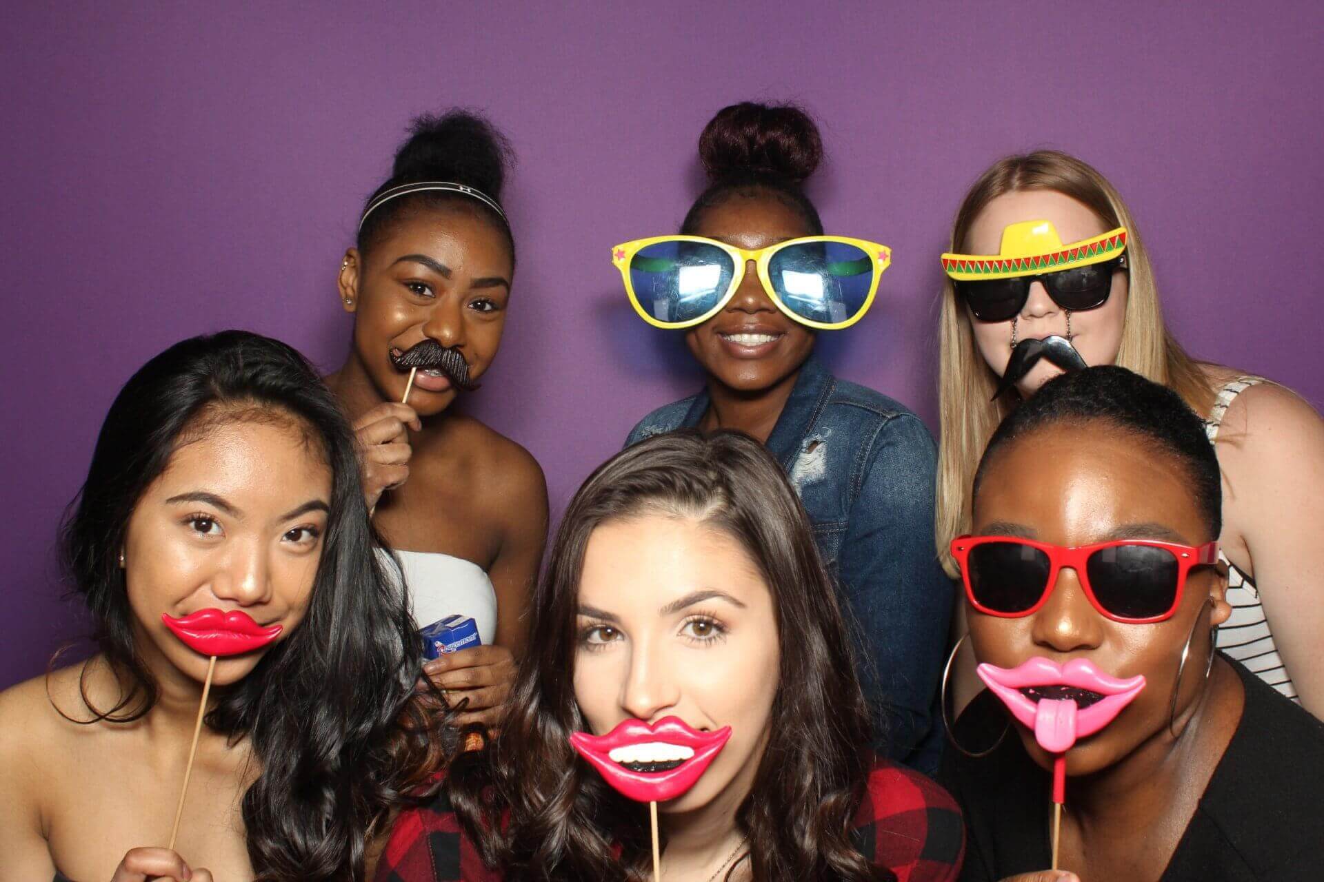 Group of people posing with photo booth props against a purple backdrop.