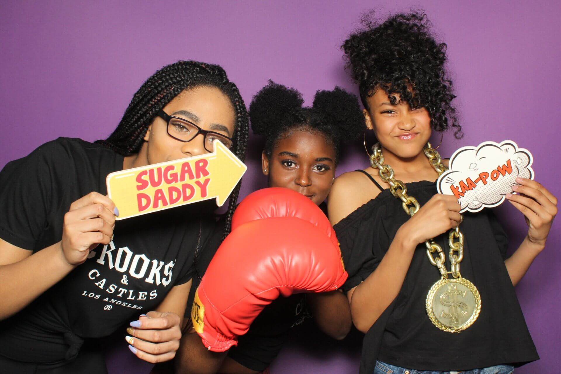 Three people pose with props in front of a purple backdrop. One holds a 