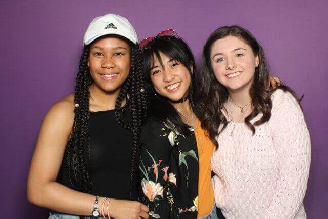 Three smiling people pose in front of a purple backdrop.