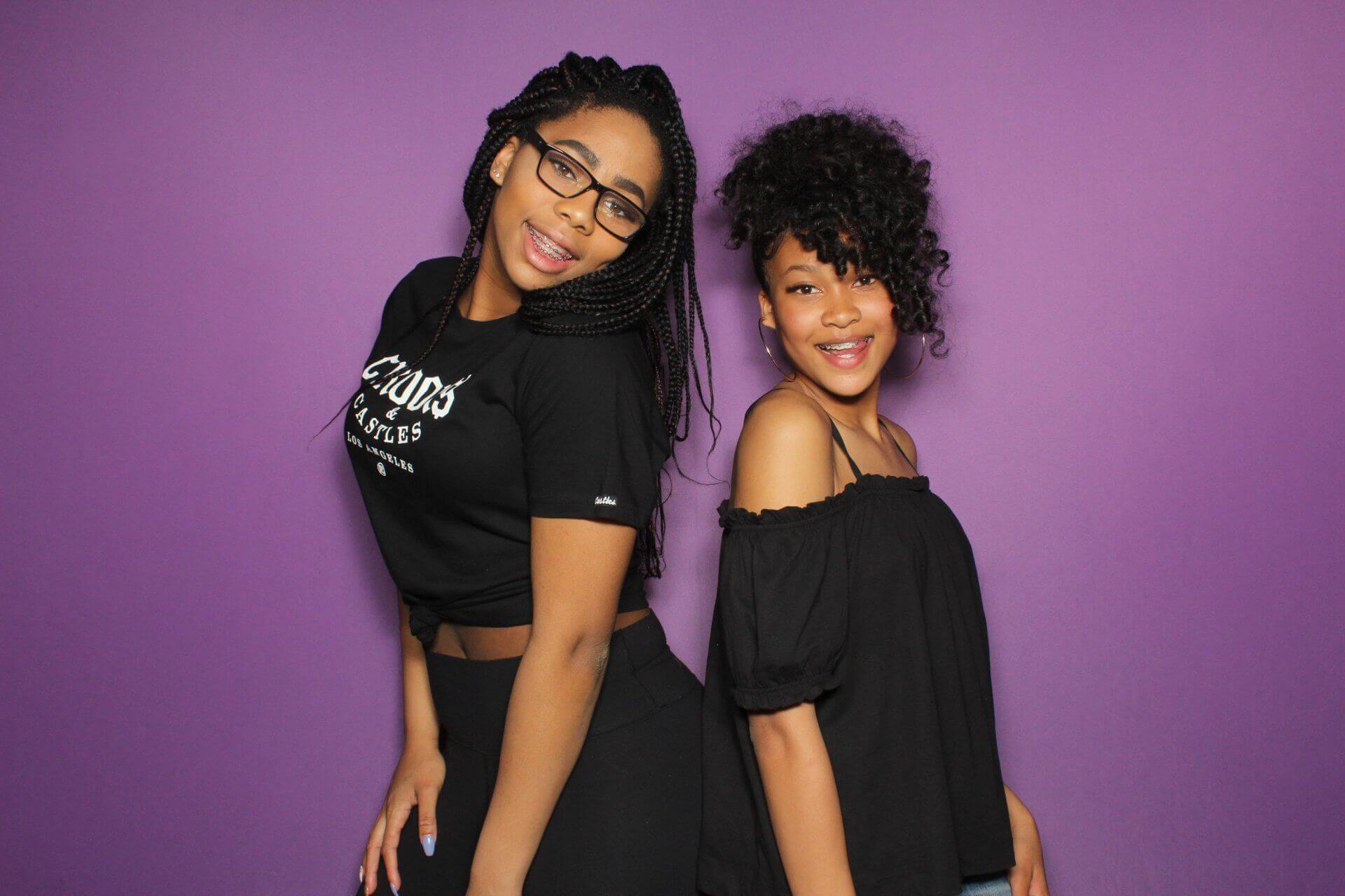 Two people smiling, posing back-to-back in front of a purple backdrop.