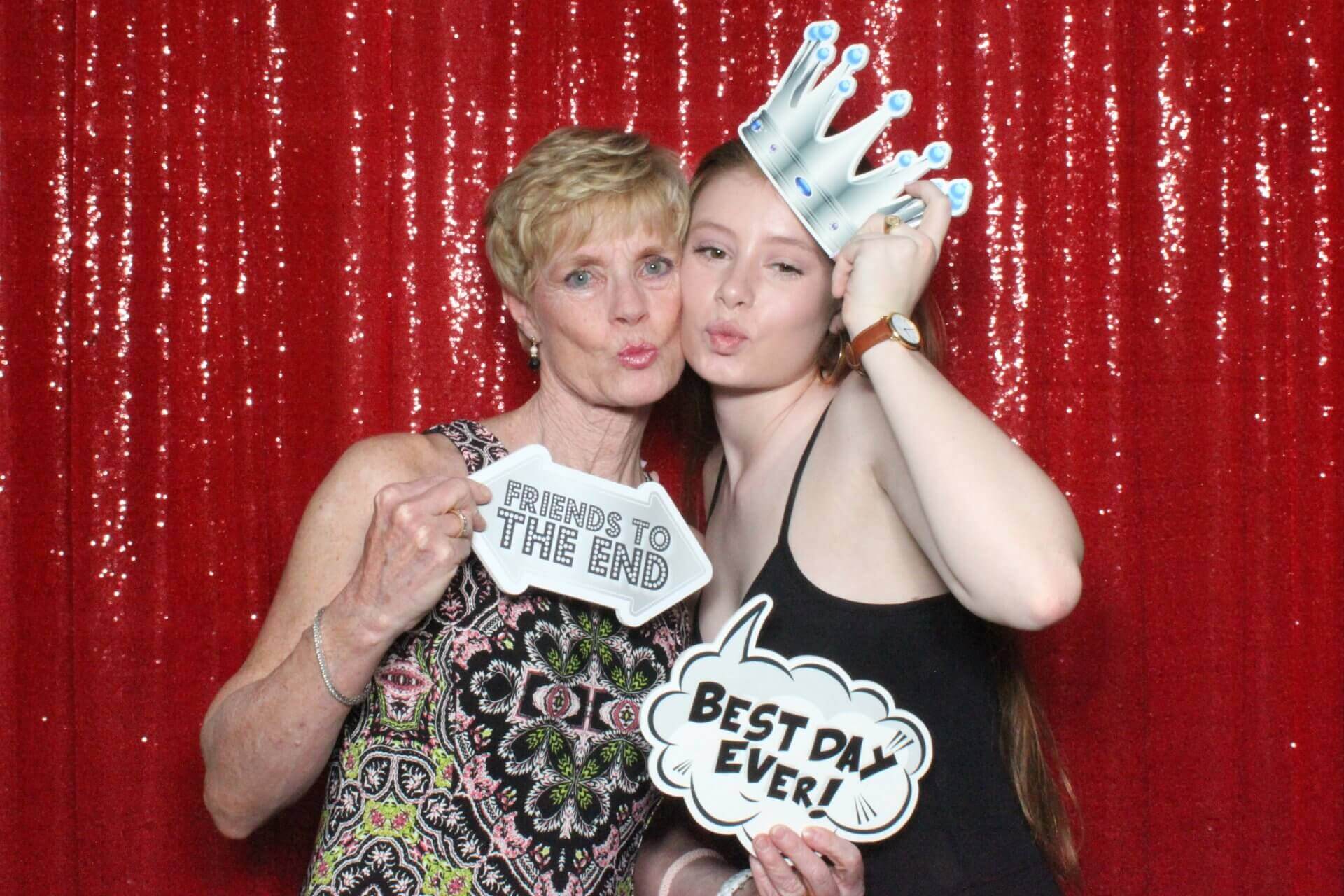Woman and young person with photo booth props; red sequined backdrop.