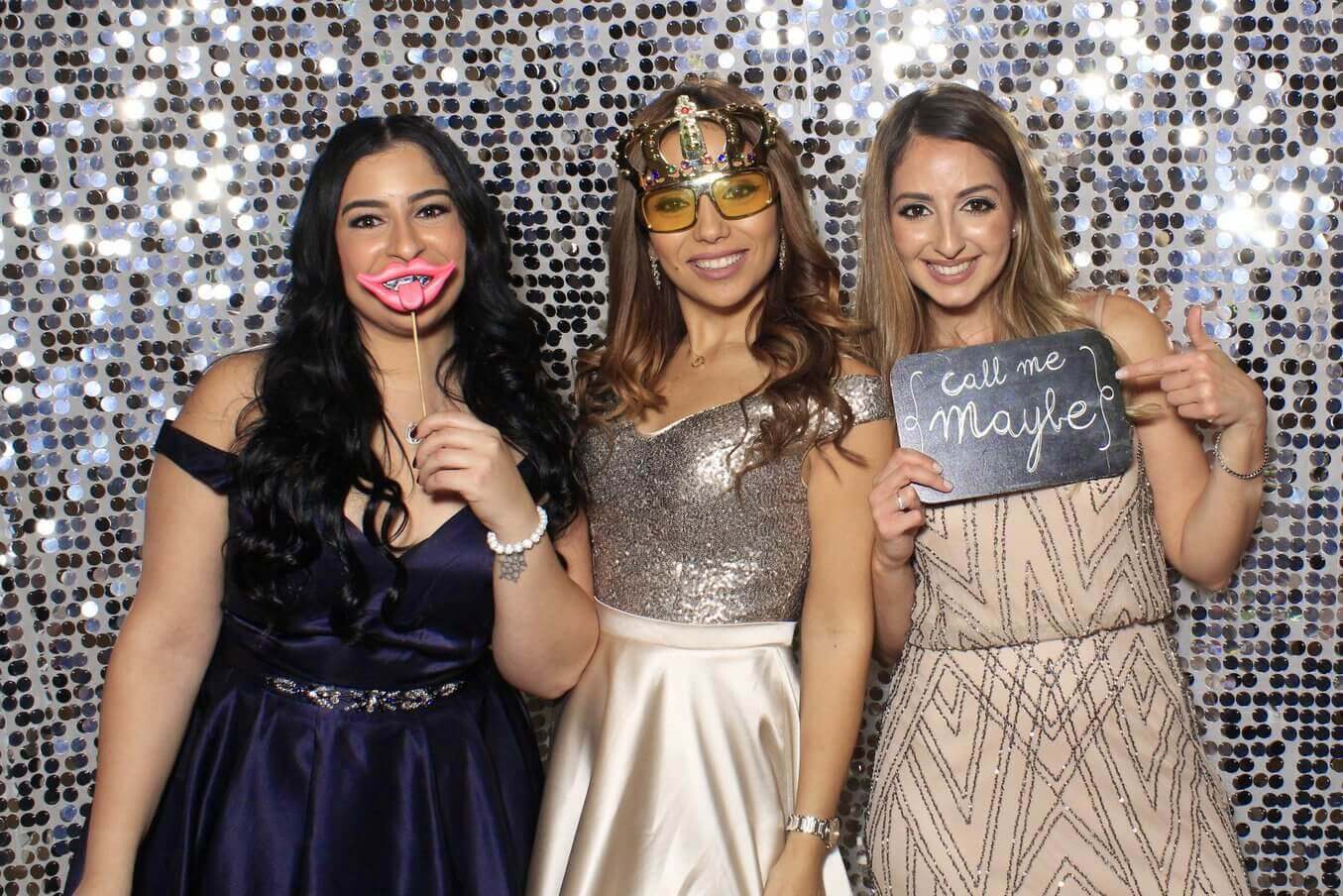 Three smiling women pose with props in front of a sparkly backdrop.