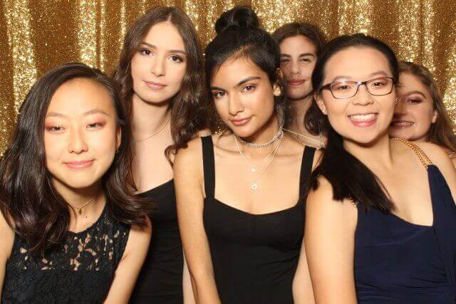 Group of young people smiling in front of a gold sequined backdrop.