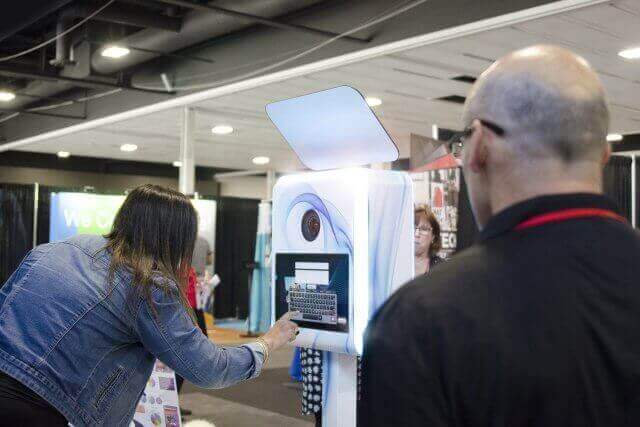 Woman interacting with photo booth touchscreen while a man watches at an event.