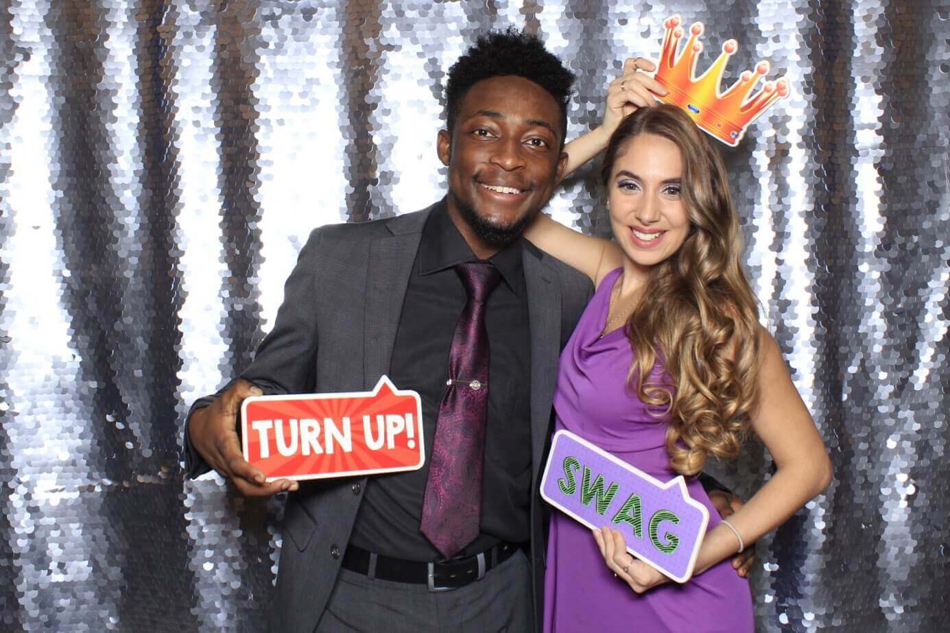 Man and woman posing at a photo booth with props against a sequined backdrop.
