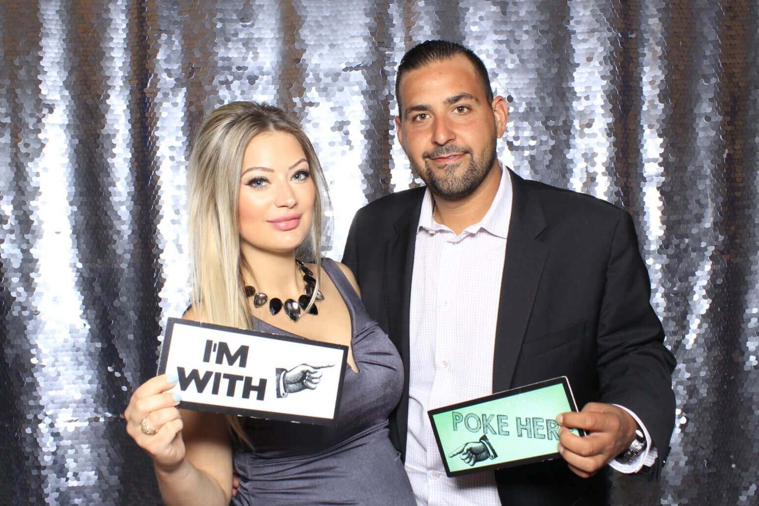 Couple in front of a sequined backdrop holding signs that read 