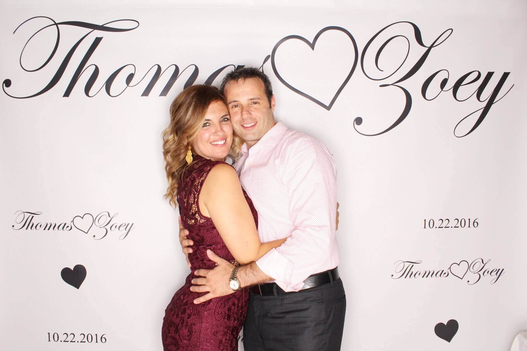 Couple embracing in front of a photo booth backdrop with their names and the date 