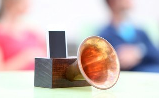 A small speaker is sitting on a table with a man in the background.