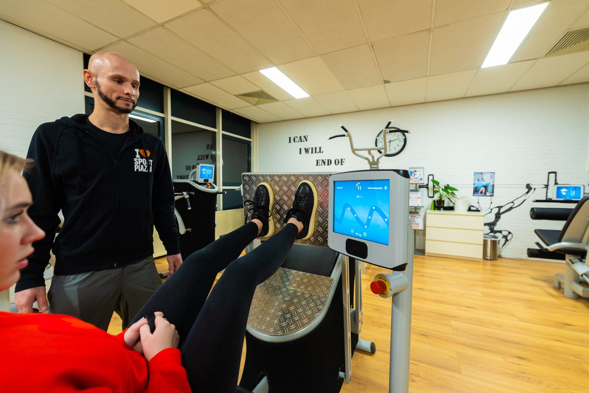 Een man staat naast een vrouw die een machine gebruikt in een sportschool.