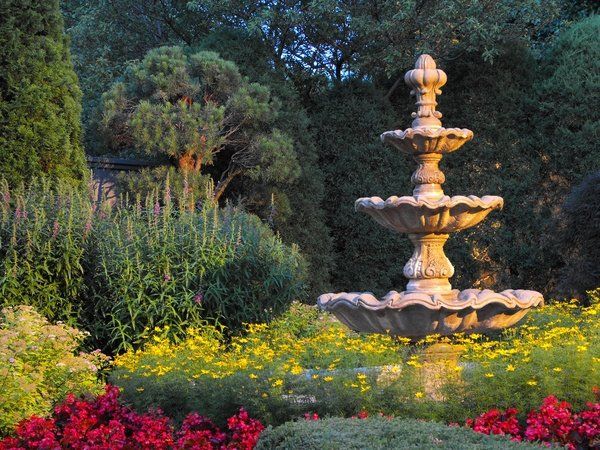 A fountain in a garden surrounded by flowers and trees