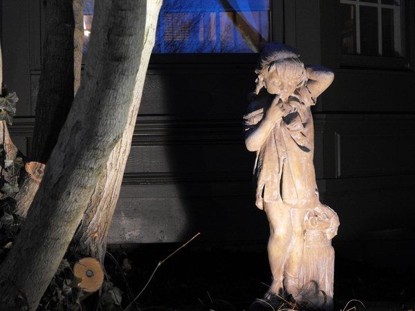 A statue of a boy standing next to a tree at night