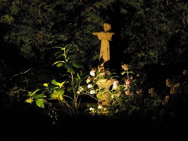 A scarecrow statue is lit up at night in a garden.