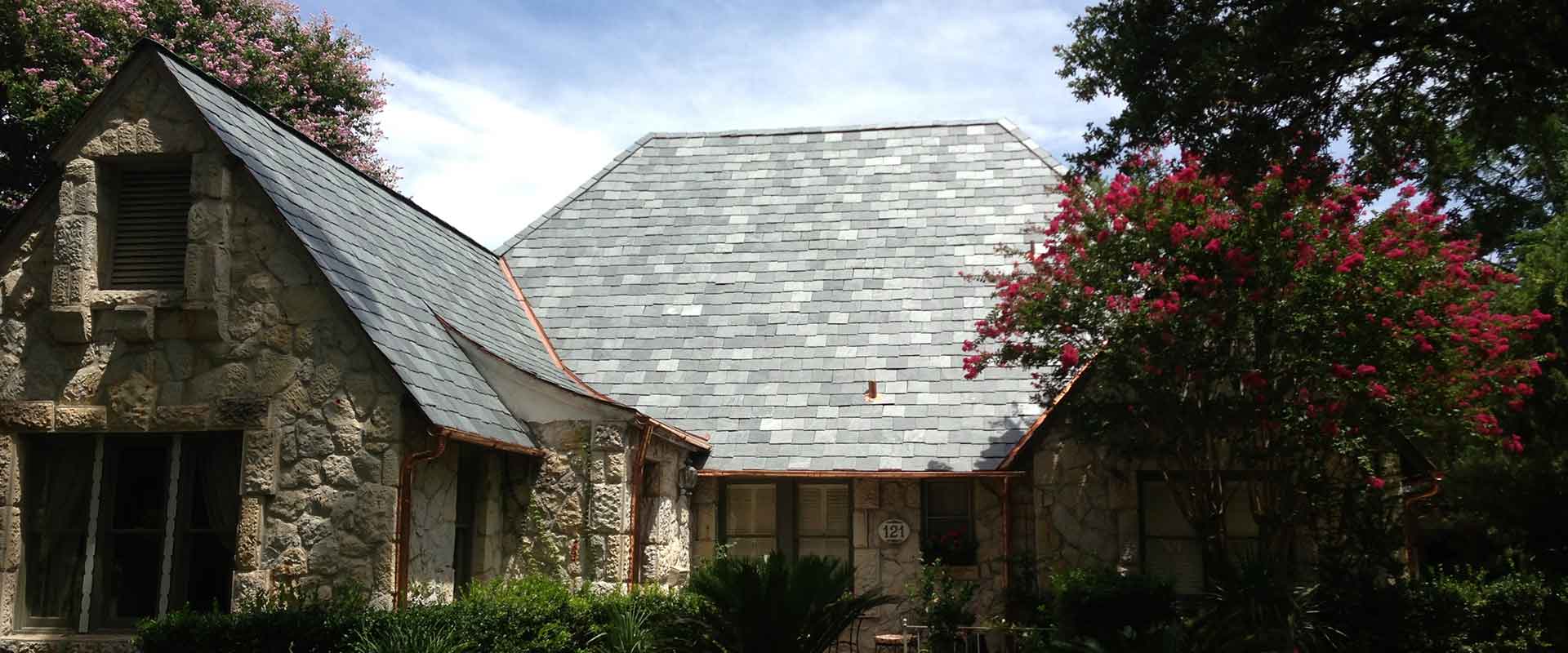 Stone house with slate roof, arched entry, and pink flowering tree in front garden