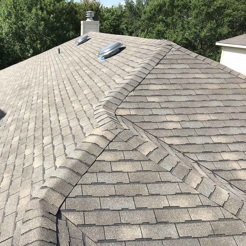 Gray shingled roof with a ridge vent and chimney under bright sunlight, viewed from above
