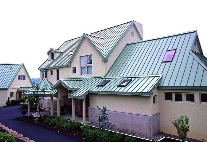 Row of beige houses with green metal roofs and small skylights on a residential street