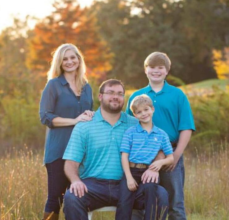 Family of four posing outdoors in field at sunset.