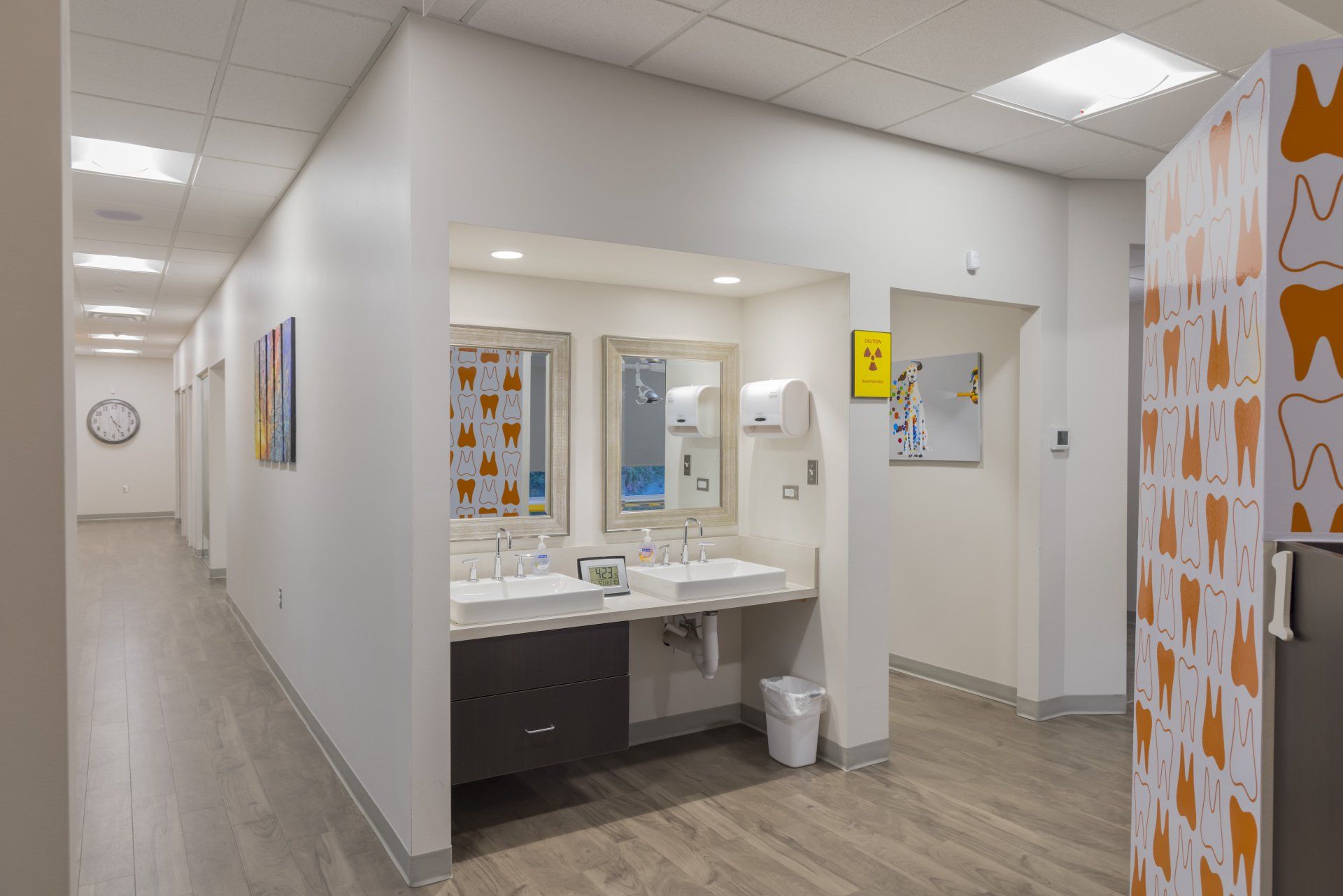 Hallway with sinks and dental-themed design. White walls, wood-look floors, and decorative screens.