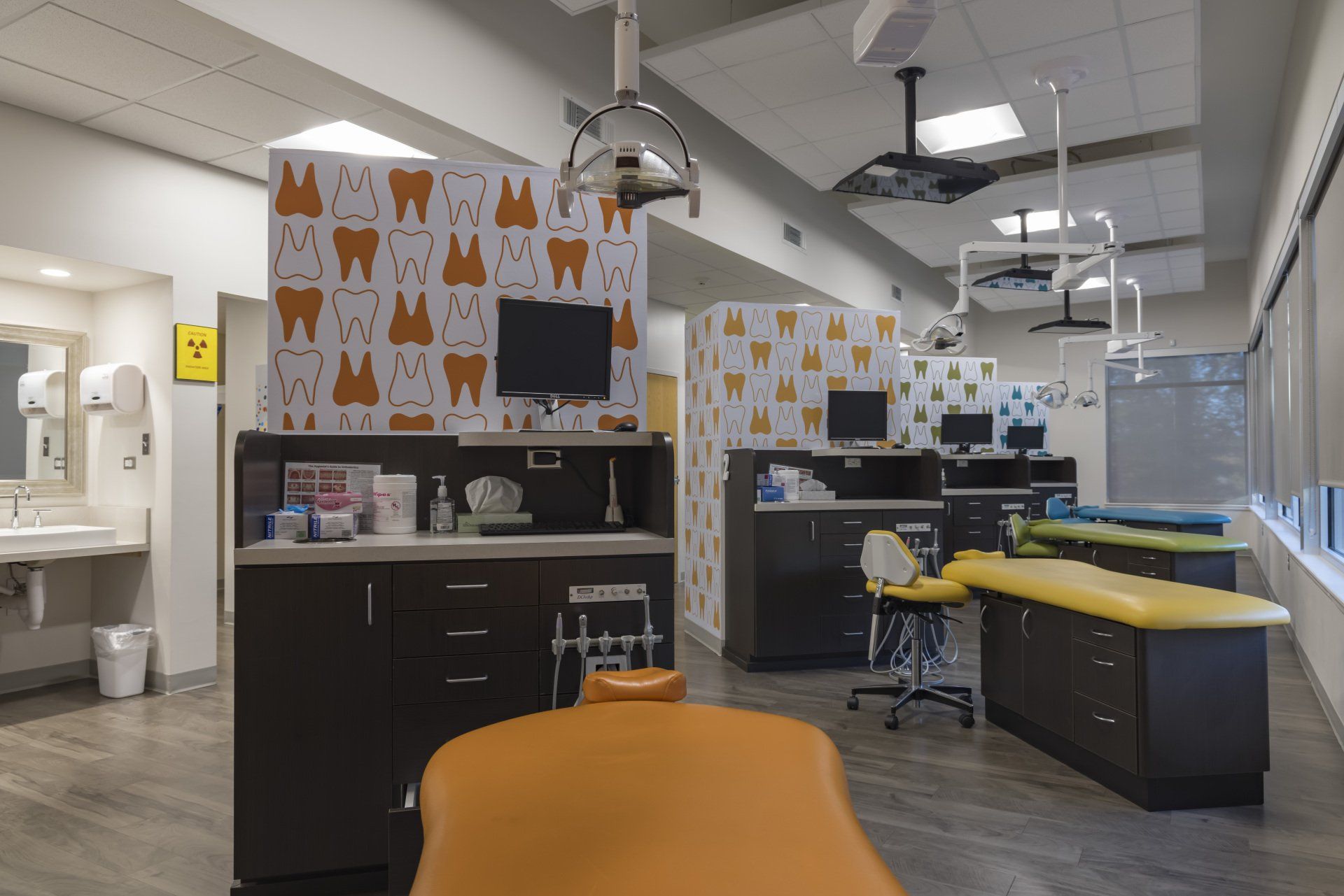 Dental office interior with dental chairs, cabinetry, and tooth-patterned wall dividers.