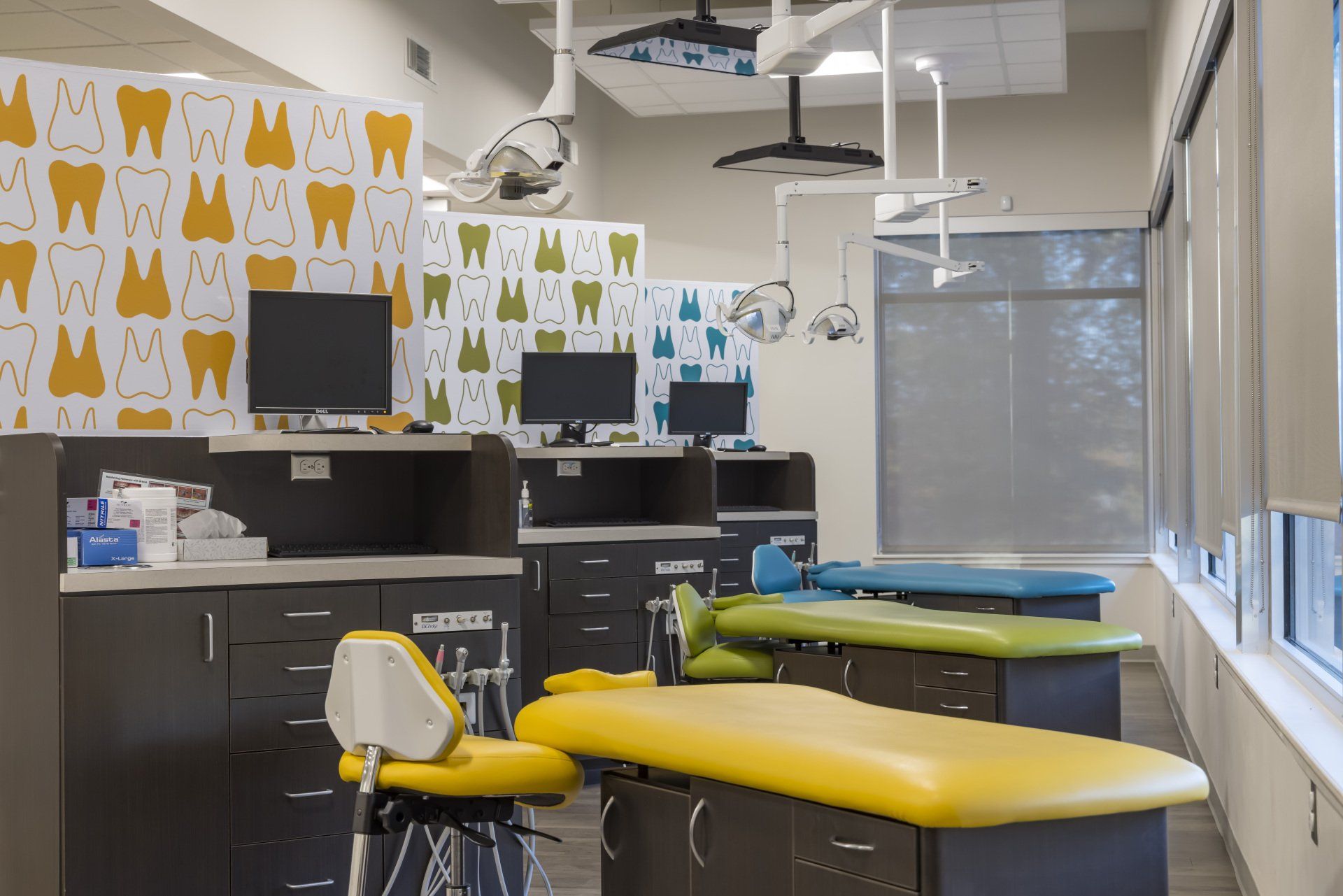 Dental office with yellow and green dental chairs, monitors, and tooth-patterned wallpaper.