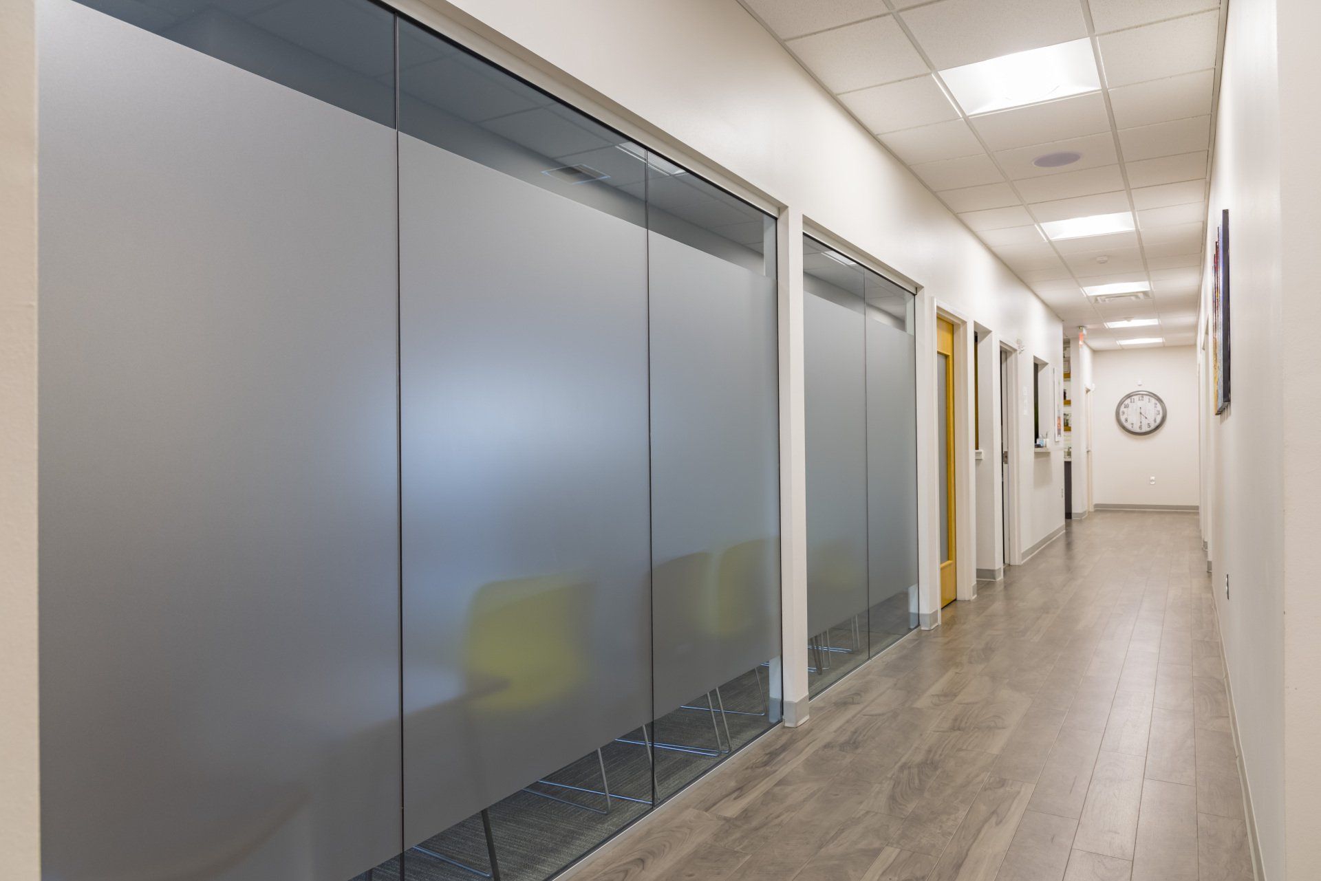 Hallway with frosted glass windows and doors, wood floor, and white walls. A clock is visible.