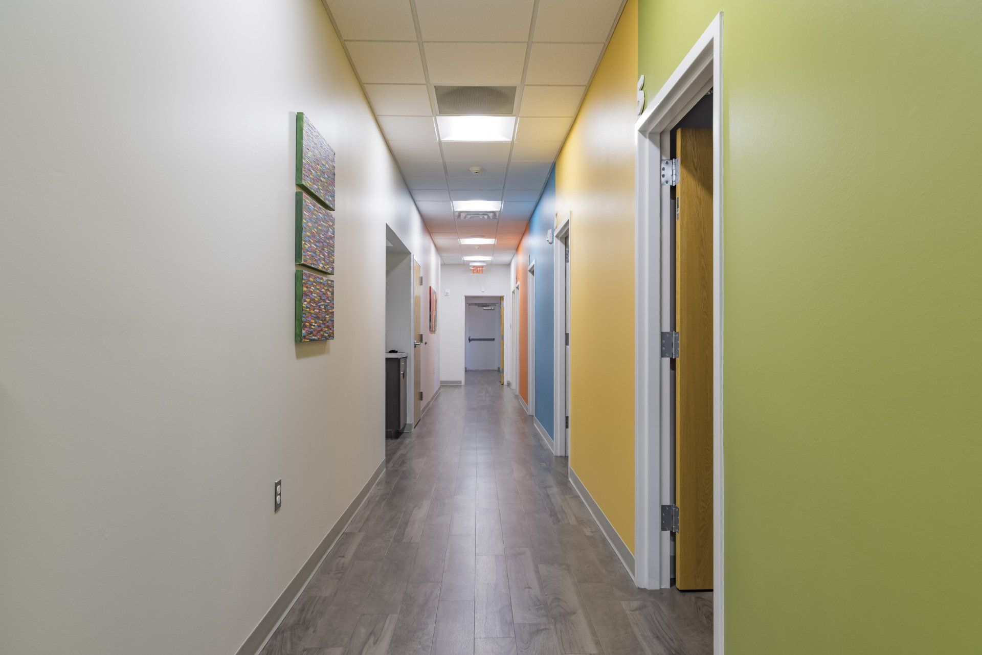 Long hallway with doors, various colored walls, and wood-look flooring.