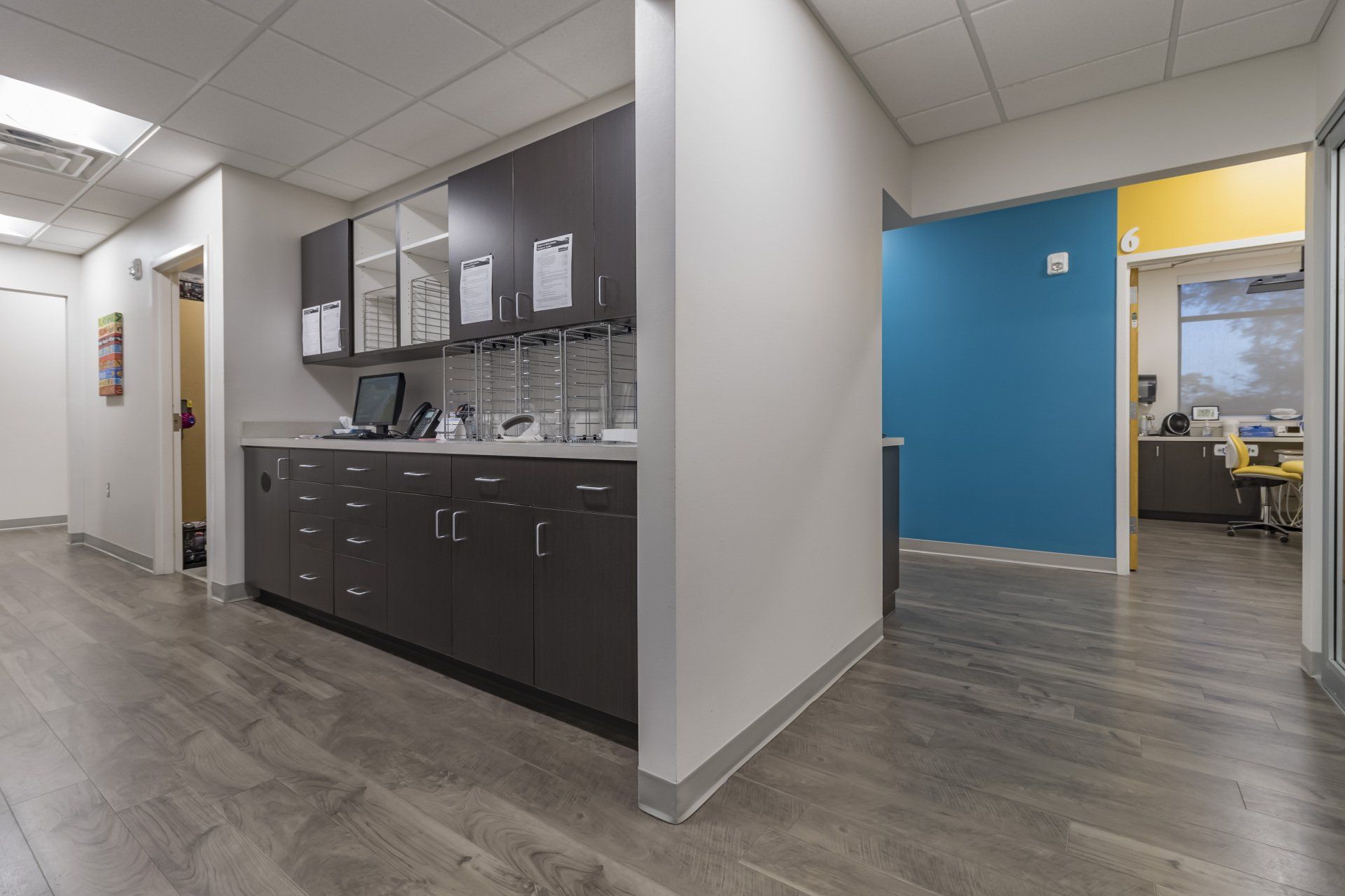 Hallway in a medical office with gray cabinets, a blue wall, and gray flooring.