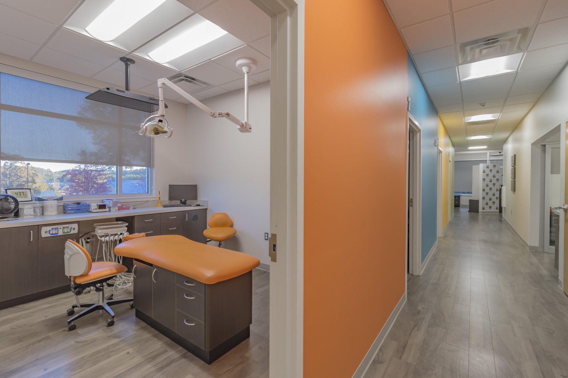 Examination room and hallway in a medical office; orange walls, medical equipment, and open doors.