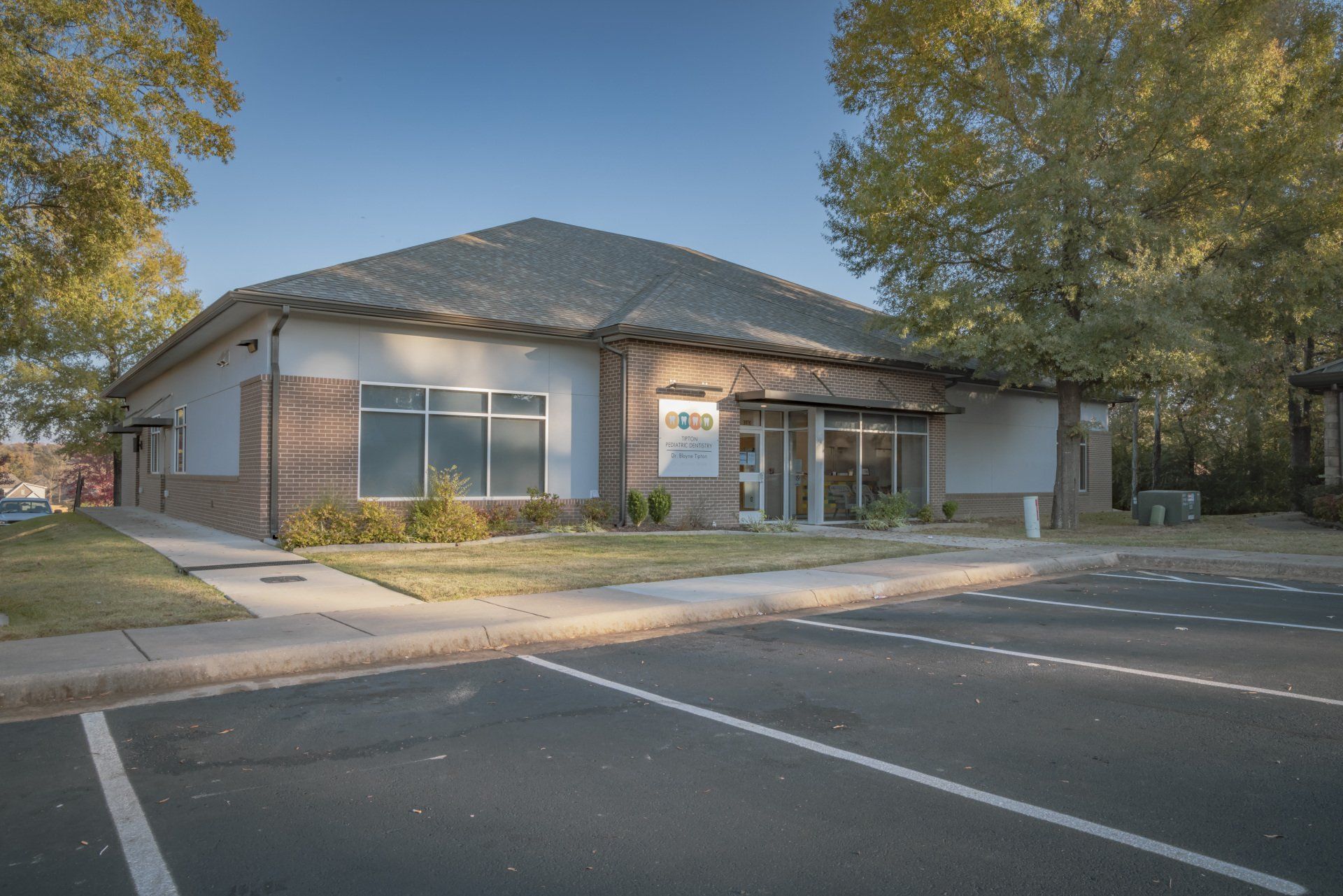 A one-story brick building with a dark gray roof on a sunny day. Parking lot in front.
