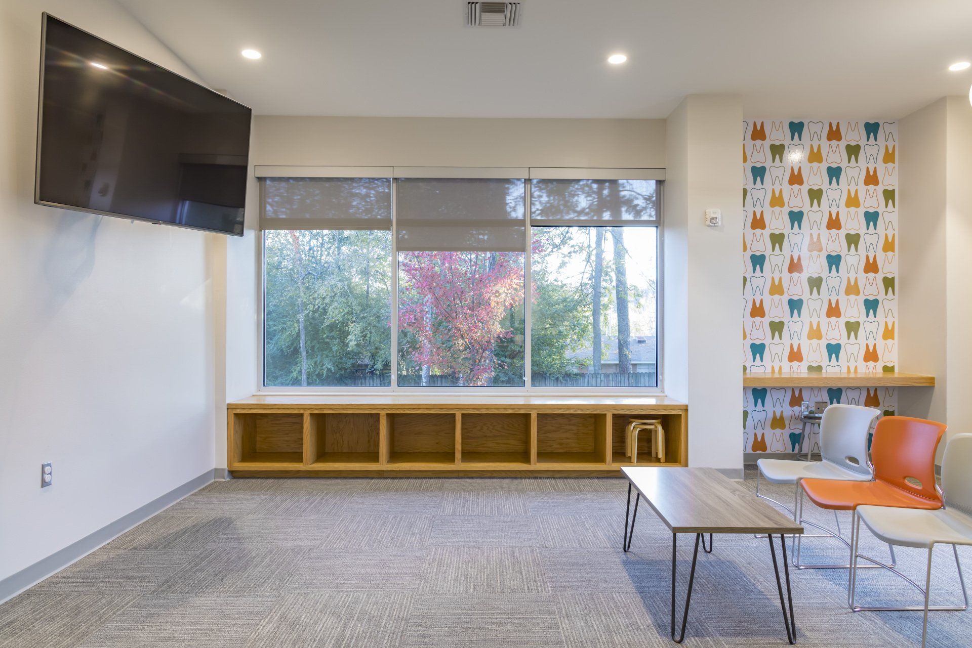 Waiting area with large window, built-in shelves, TV, and colorful tooth-patterned accent wall.