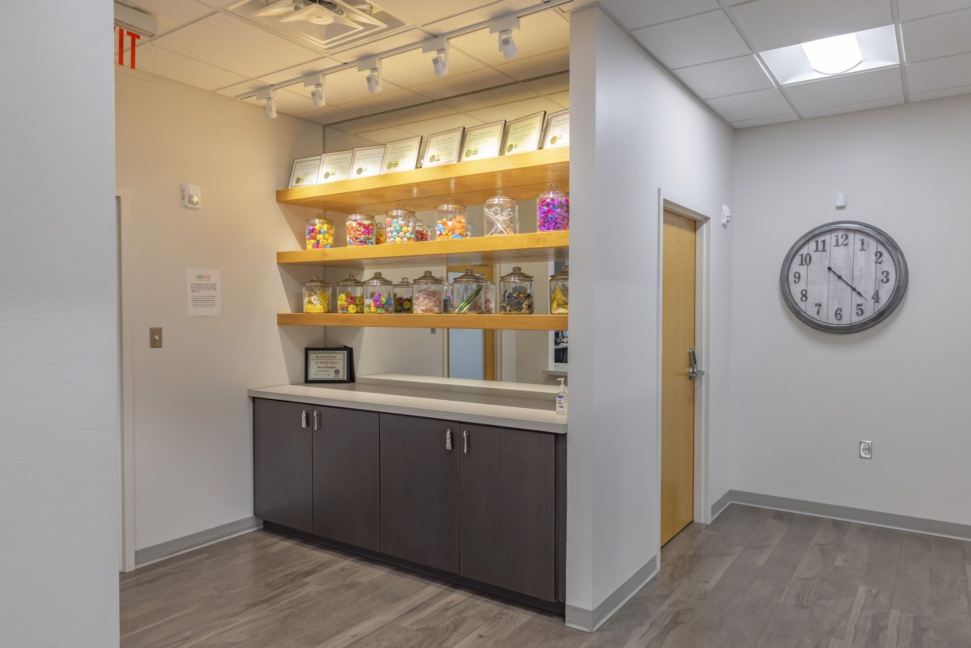 Reception area with candy jars on shelves, cabinet, clock on wall, and door.