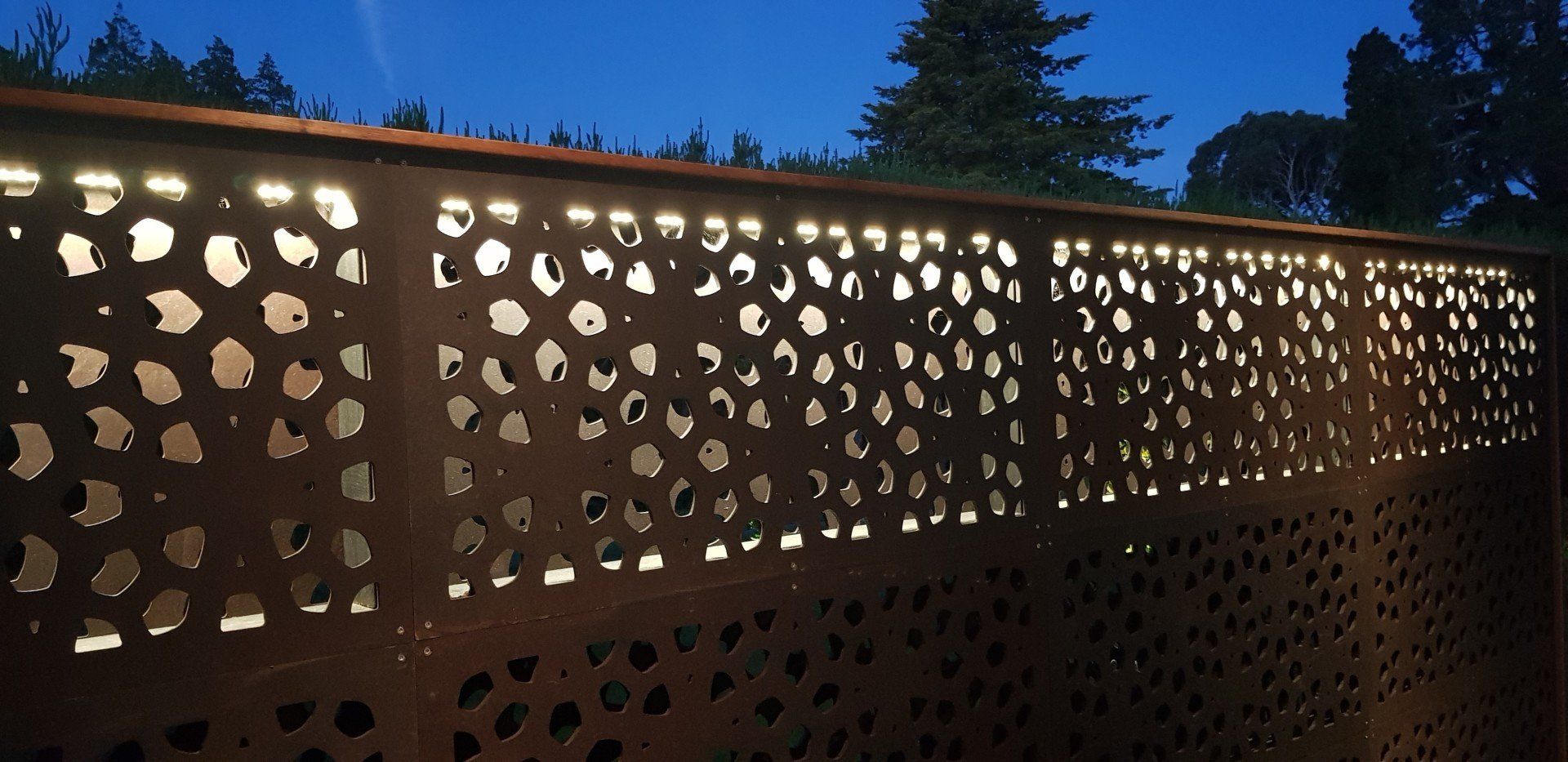 A metal fence with holes in it is lit up at night.
