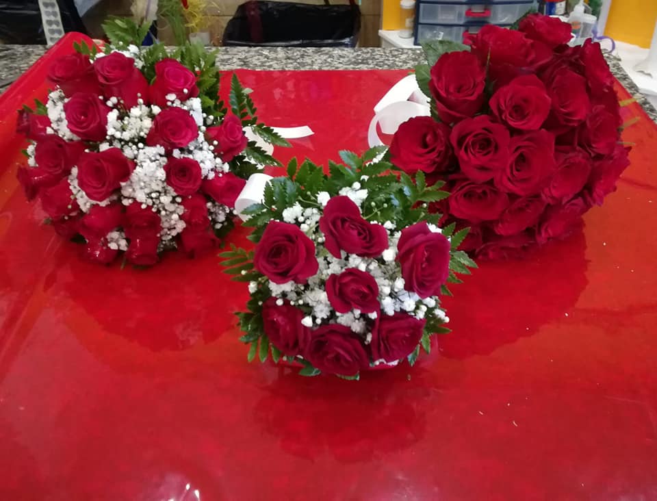 Tre bouquet di rose rosse su una superficie rossa, impreziositi da gypsophila bianca e verde.