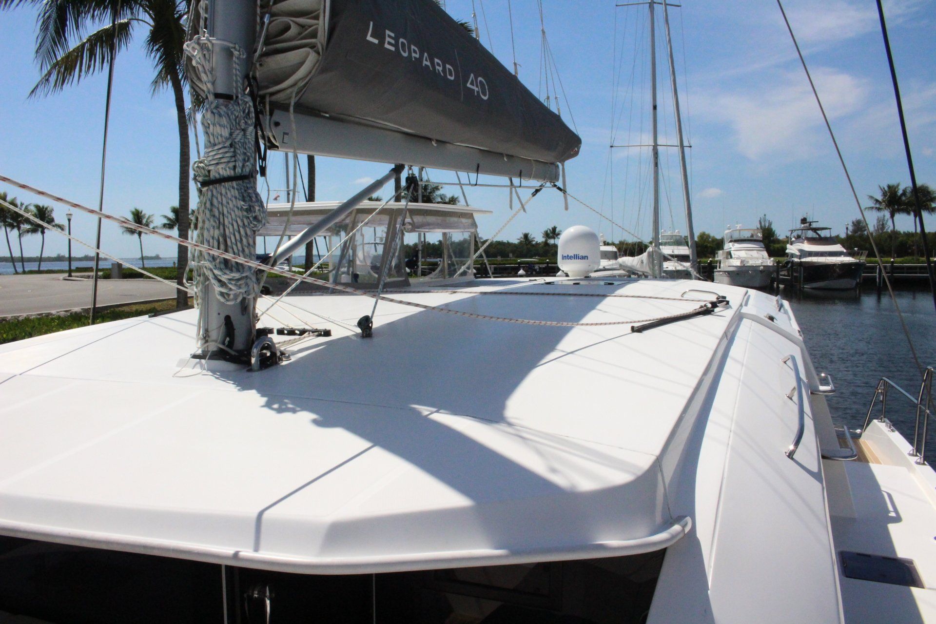 A white sailboat is docked in a marina with palm trees in the background.