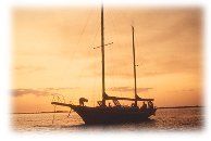 A sailboat is floating on top of a body of water at sunset.