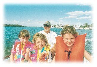 A man and three girls are on a boat wearing life jackets