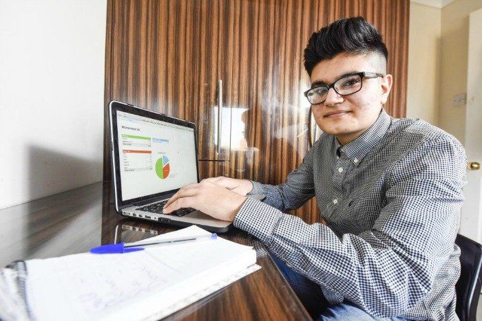 A young man is sitting at a desk using a laptop computer.