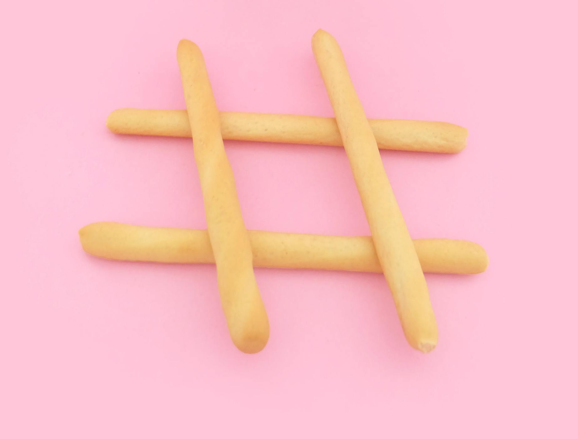 A hashtag sign made out of bread sticks on a pink background.