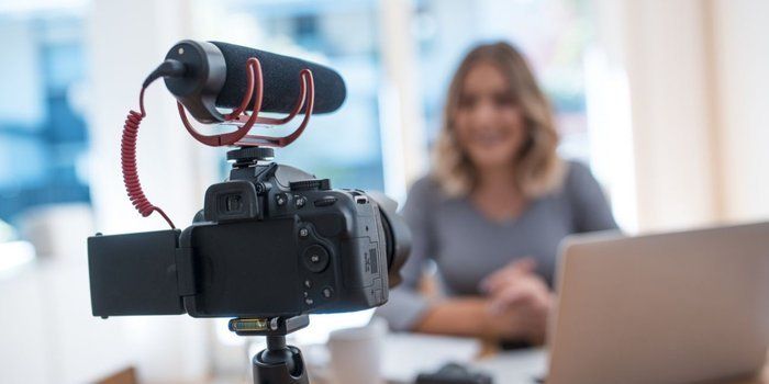 A woman is sitting at a table being filmed by a camera.