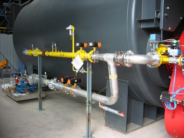 Industrial equipment with yellow and silver pipes against a large, dark cylindrical tank.