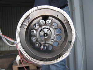 Close-up of a circular industrial component with multiple holes, surrounded by a metallic braided covering.