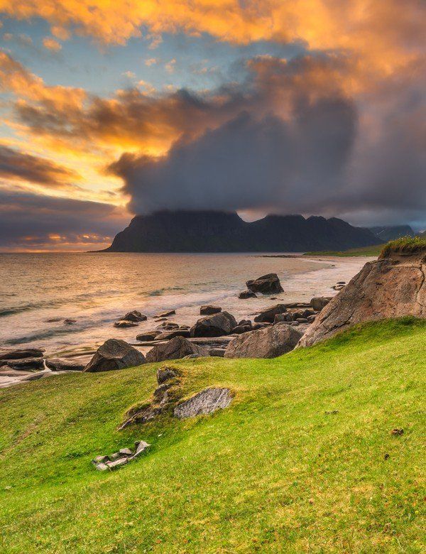 A sunset over a rocky beach with mountains in the background.