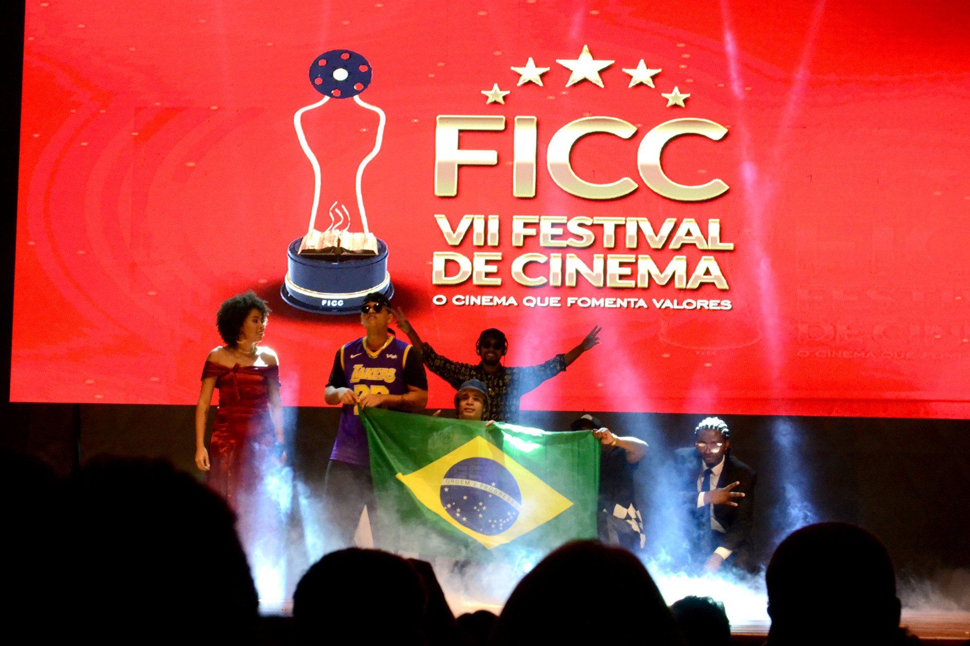 Um grupo de pessoas em pé em frente a uma tela que diz ficc vii festival de cinema